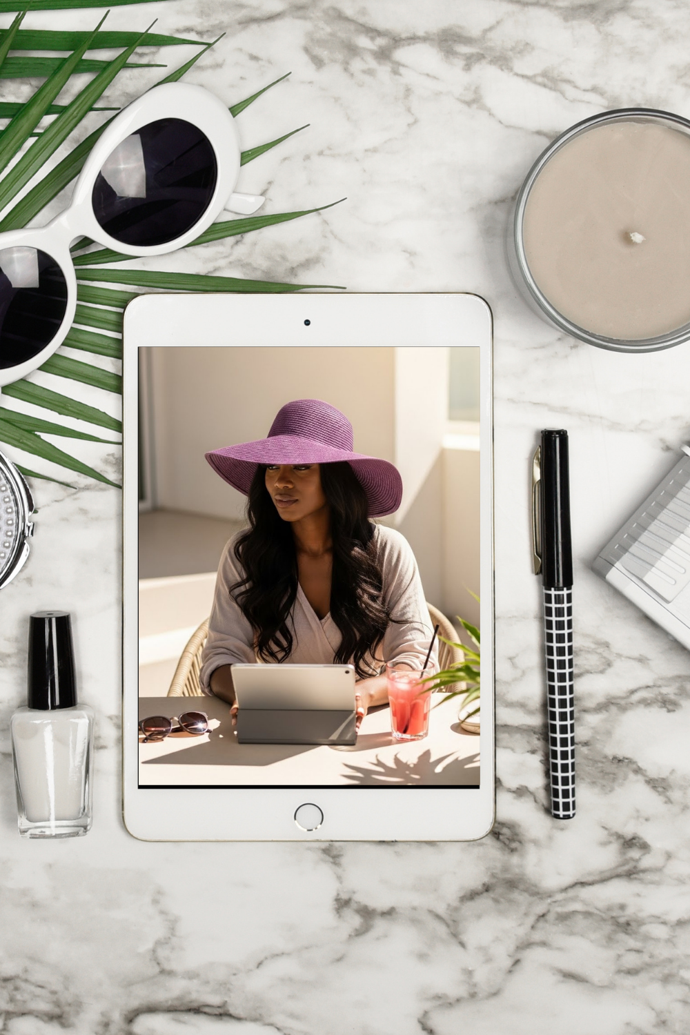 Tablet displaying a woman on a video call with sunglasses, candle, and other items on a marble surface.